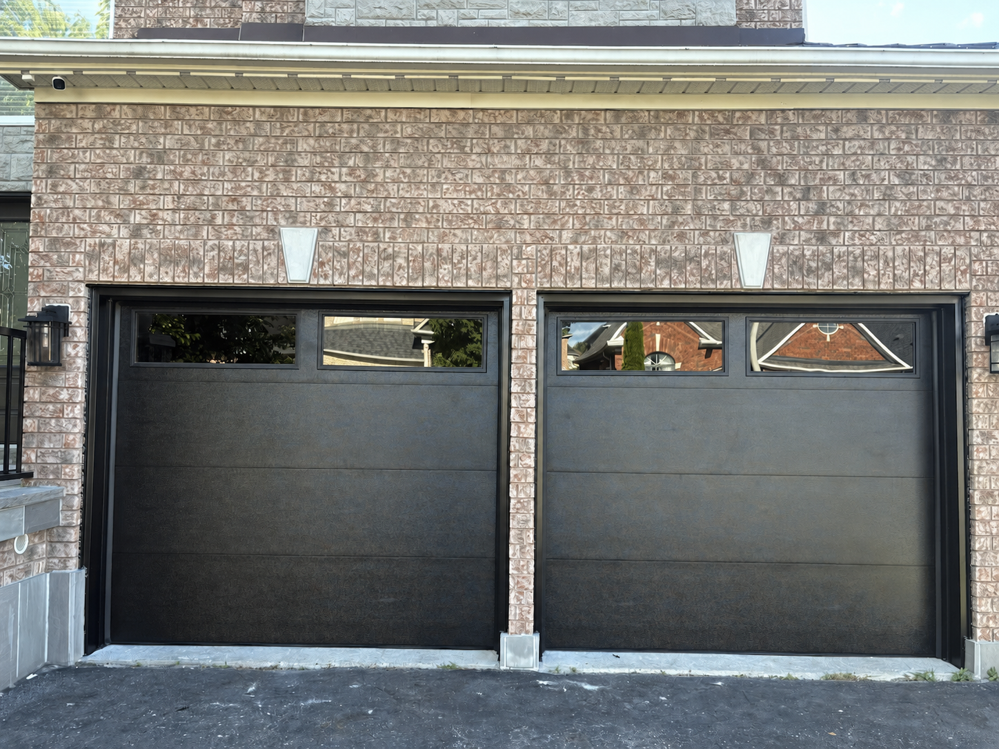 After — two matching matte black garage doors with tinted privacy glass, black-capped frames, set into the stone and brick facade