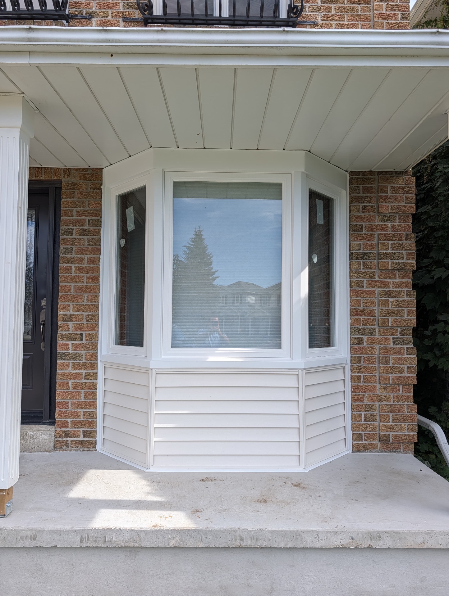 New white bay window with vinyl siding skirt and capping finished cleanly against a brick front wall