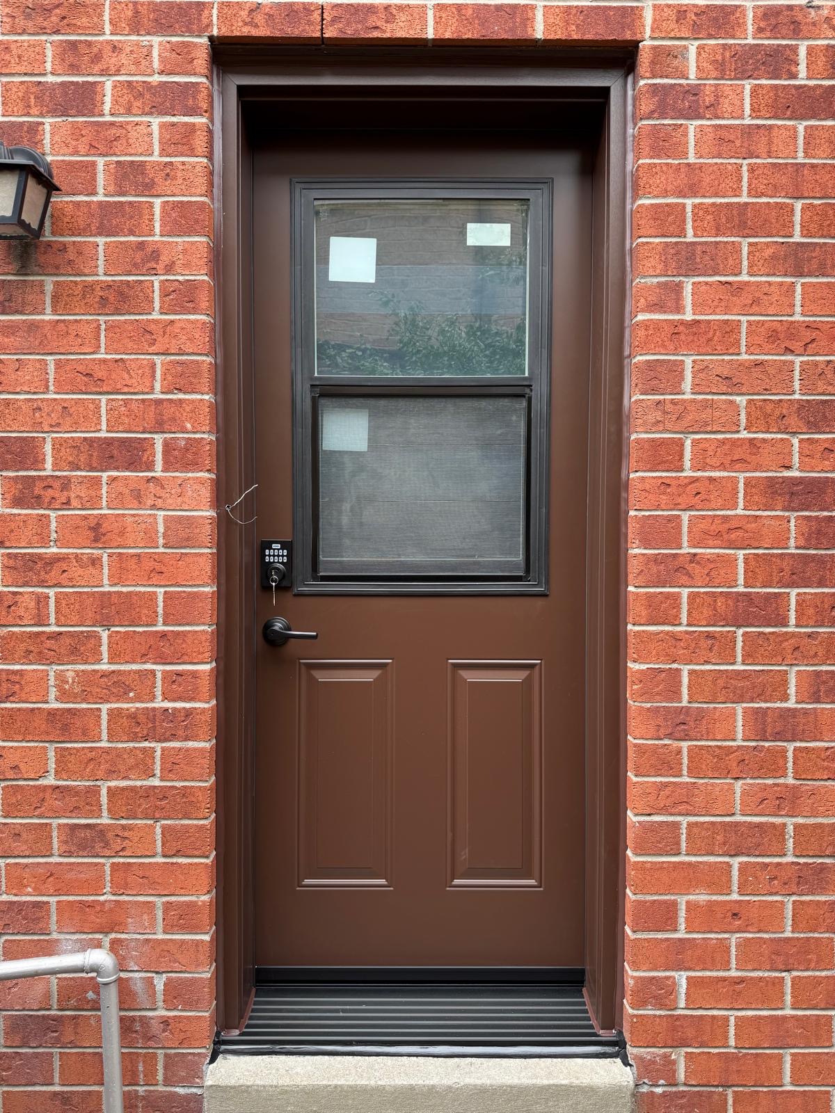 Brown steel entry door with an upper glass insert installed in a red brick wall