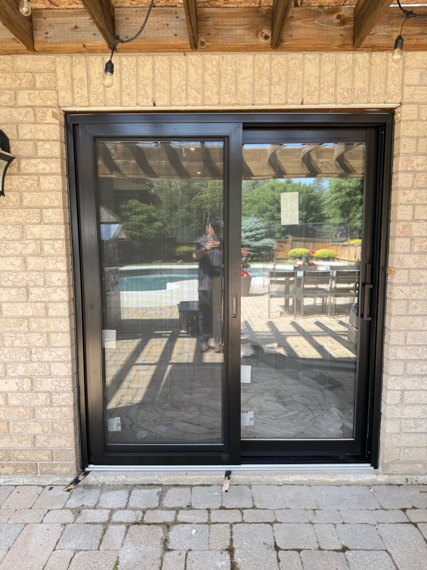 Black sliding patio door installed in a brick opening beside an outdoor pool