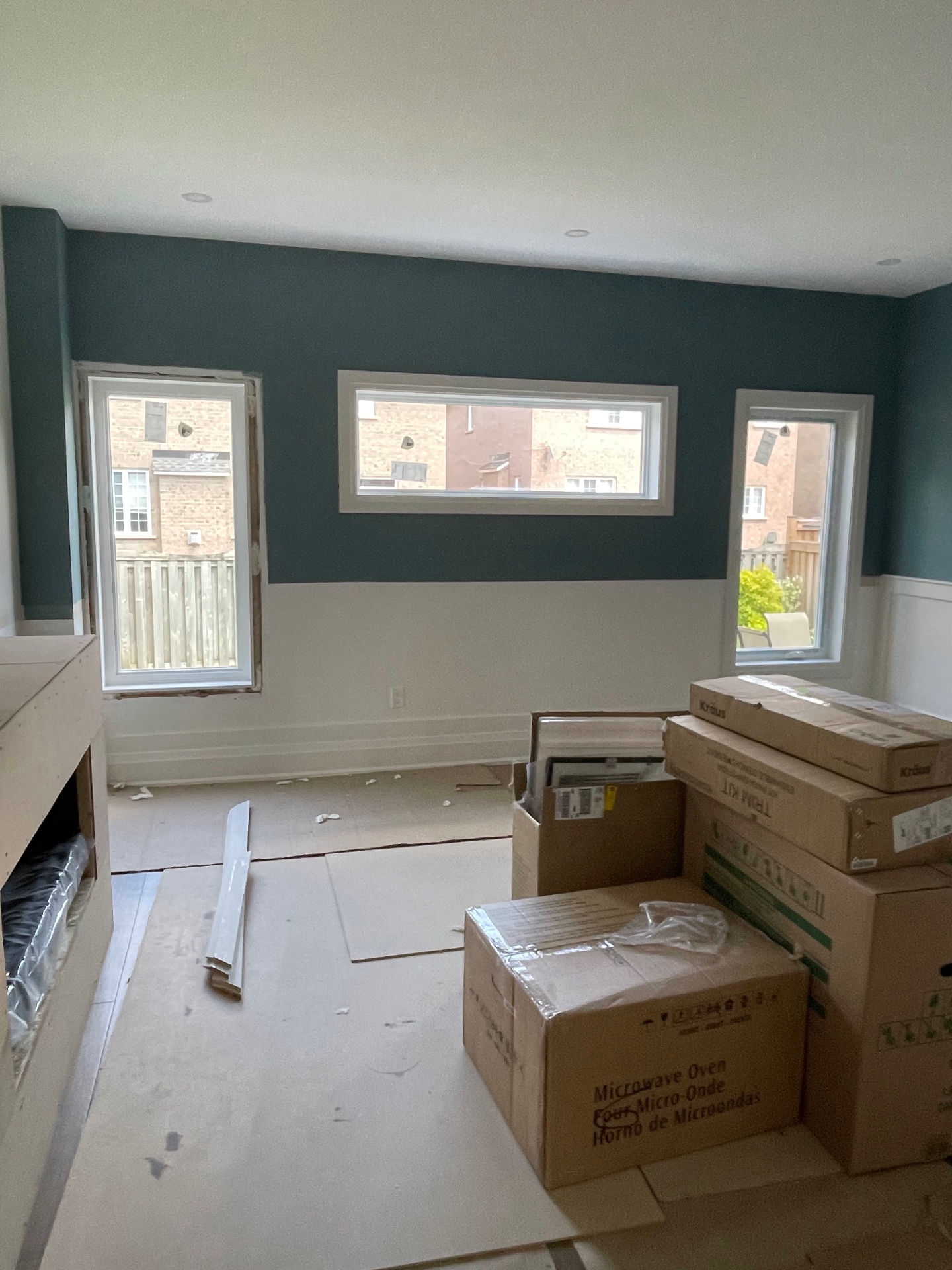 Family room during installation — the right-side window already installed and finished with stepped wood casing while the left opening is still bare
