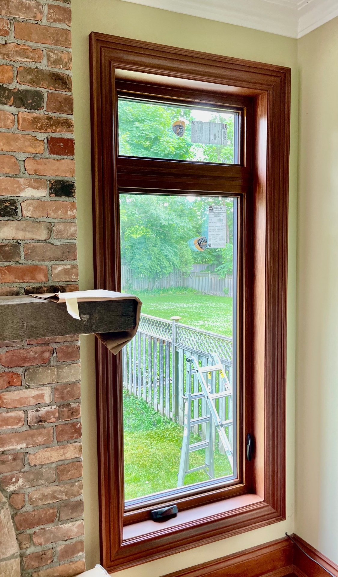 Dark stained wood colonial window casing framing a casement-over-awning window against an exposed brick wall in an Ontario heritage home