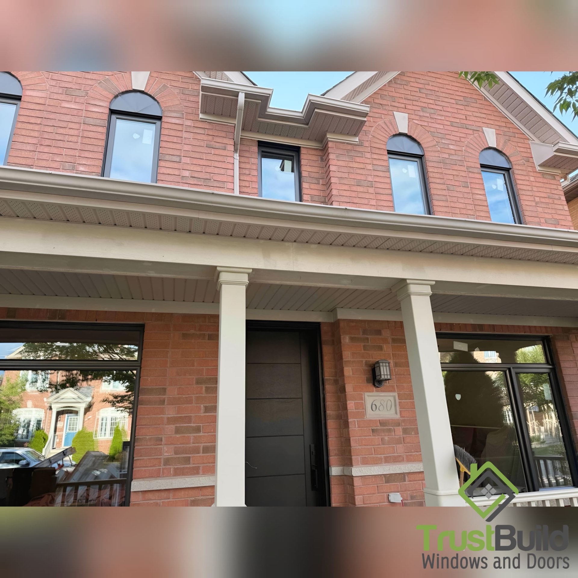 Black-frame windows and a modern black entry door installed in a red brick Oakville home, showing arched brick openings and finished masonry above each window