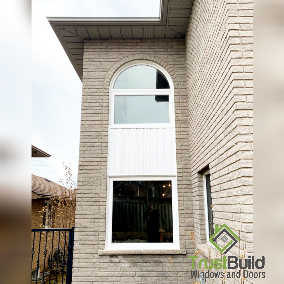 Tall arched white vinyl window with a spandrel panel installed in a beige brick two-storey Ontario home