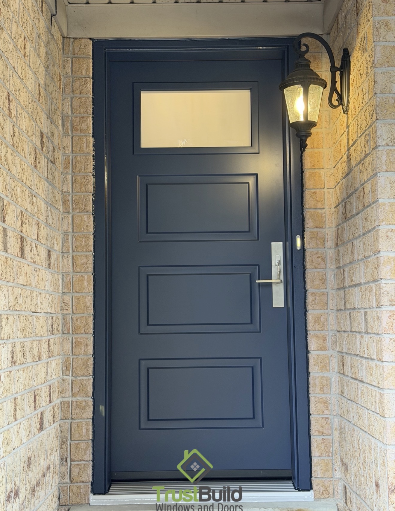 After — navy blue steel entry door with a rectangular frosted glass insert, brushed nickel Ferco Roma multipoint lock, matching silver aluminum threshold